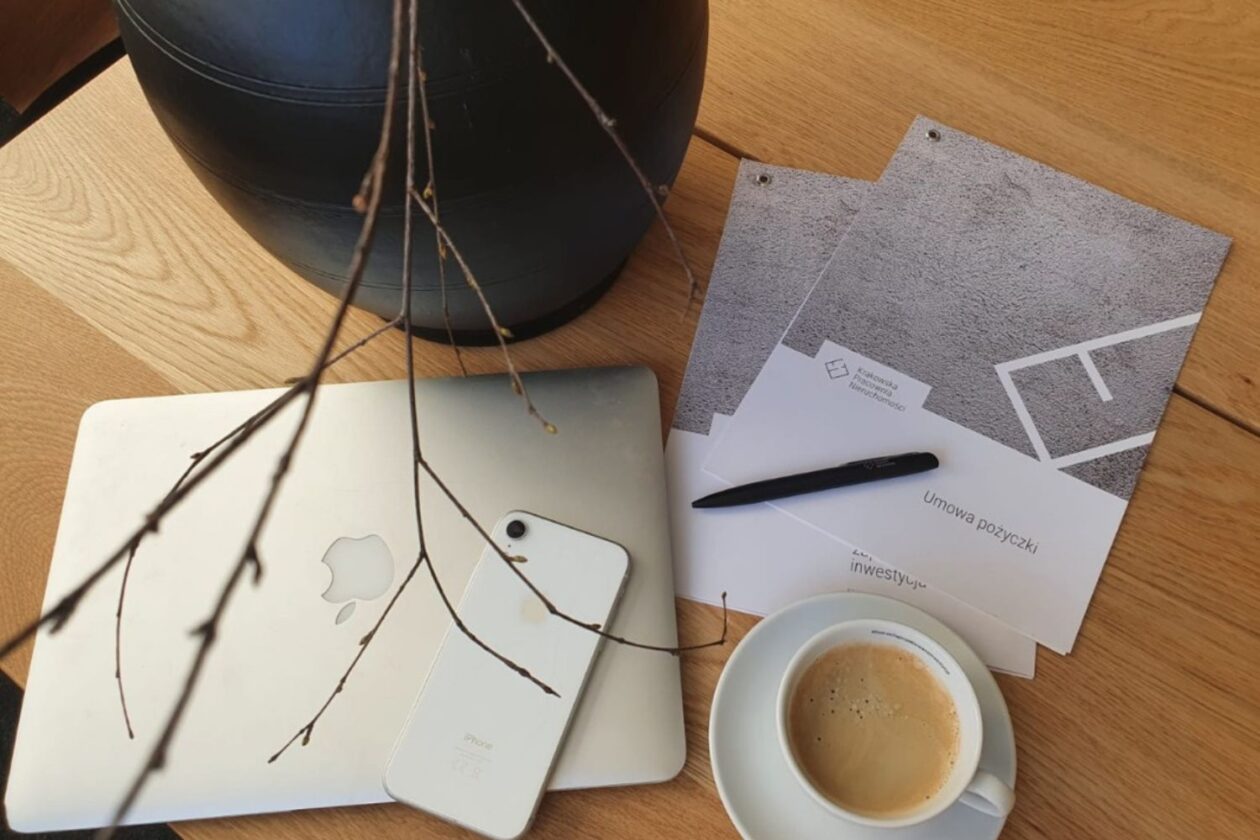 Zdjęcie stołu, na którym położony jest laptop, telefon oraz kawa i umowa o pożyczkę inwestycyjną.