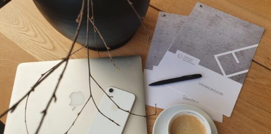 Zdjęcie stołu, na którym położony jest laptop, telefon oraz kawa i umowa o pożyczkę inwestycyjną.