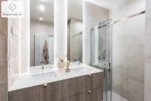 Mieszkanie na sprzedaż Kraków Bronowice - nowoczesna łazienka wykończona jasnymi płytkami, z podwójną umywalką, dużym lustrem z oświetleniem LED oraz prysznicem z przeszklonymi drzwiami
